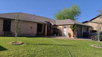 A residential house with a brick exterior, a front door, a garage, and a well-maintained lawn.