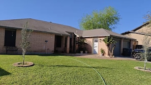 A residential house with a brick exterior, a front door, a garage, and a well-maintained lawn. - El Encanto Studio (Laredo)