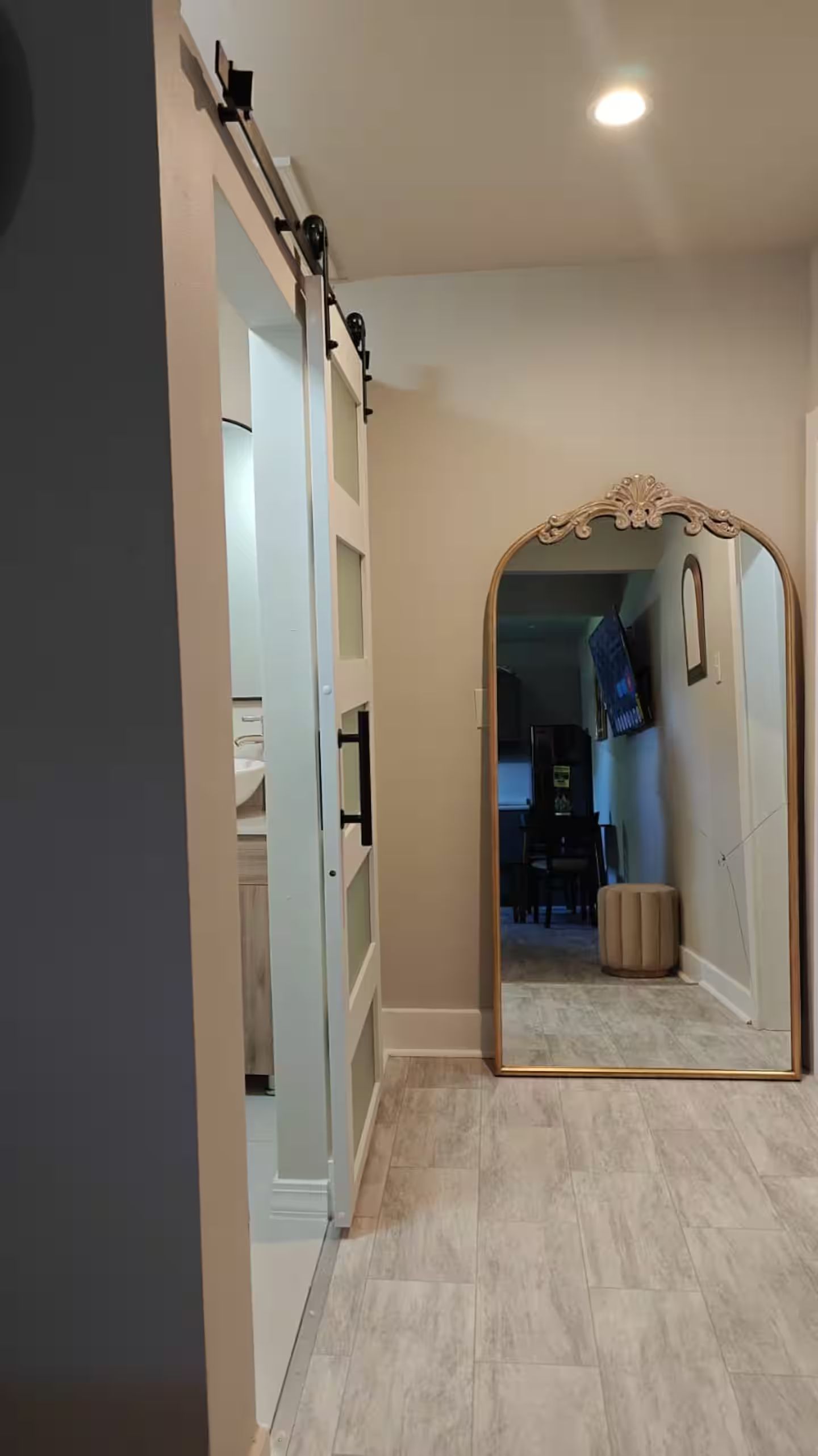 A hallway with a mirrored wall and a sliding door leading to a room with a desk and chair.