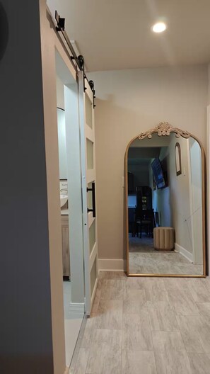 A hallway with a mirrored wall and a sliding door leading to a room with a desk and chair. - El Encanto Studio (Laredo)