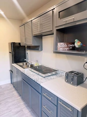 A kitchen with grey cabinets, a black refrigerator, a built-in stove, a sink, and a toaster. - El Encanto Studio (Laredo)