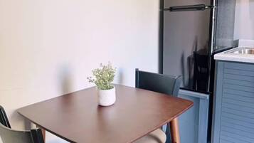 A small dining area with a table and chairs, a potted plant, and a refrigerator in the background.
