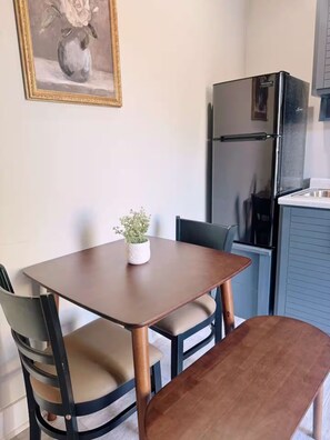 A small dining area with a table and chairs, a potted plant, and a refrigerator in the background. - El Encanto Studio (Laredo)