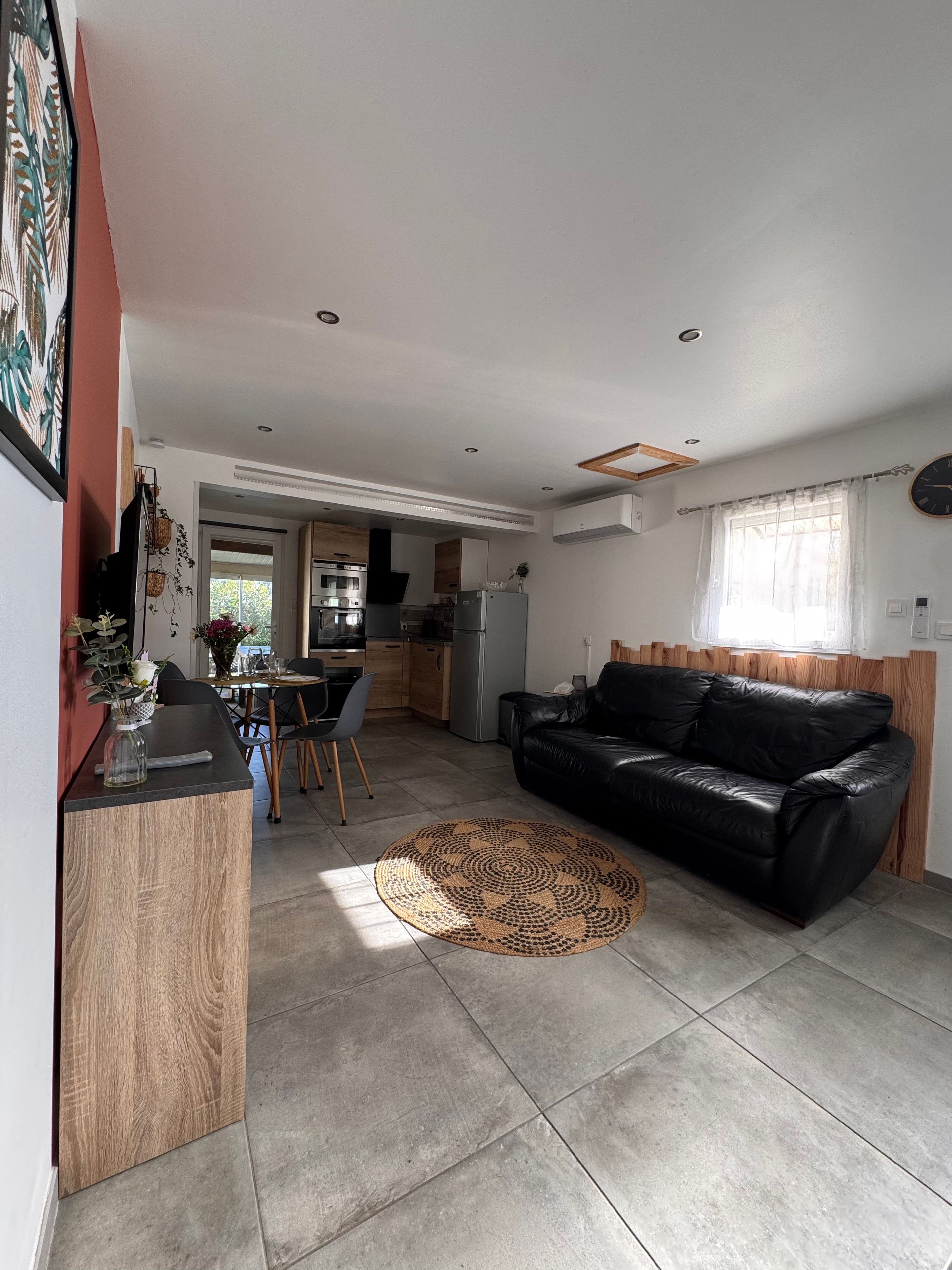 A modern living room with a black leather sofa, a dining area with chairs, and a kitchen in the background.