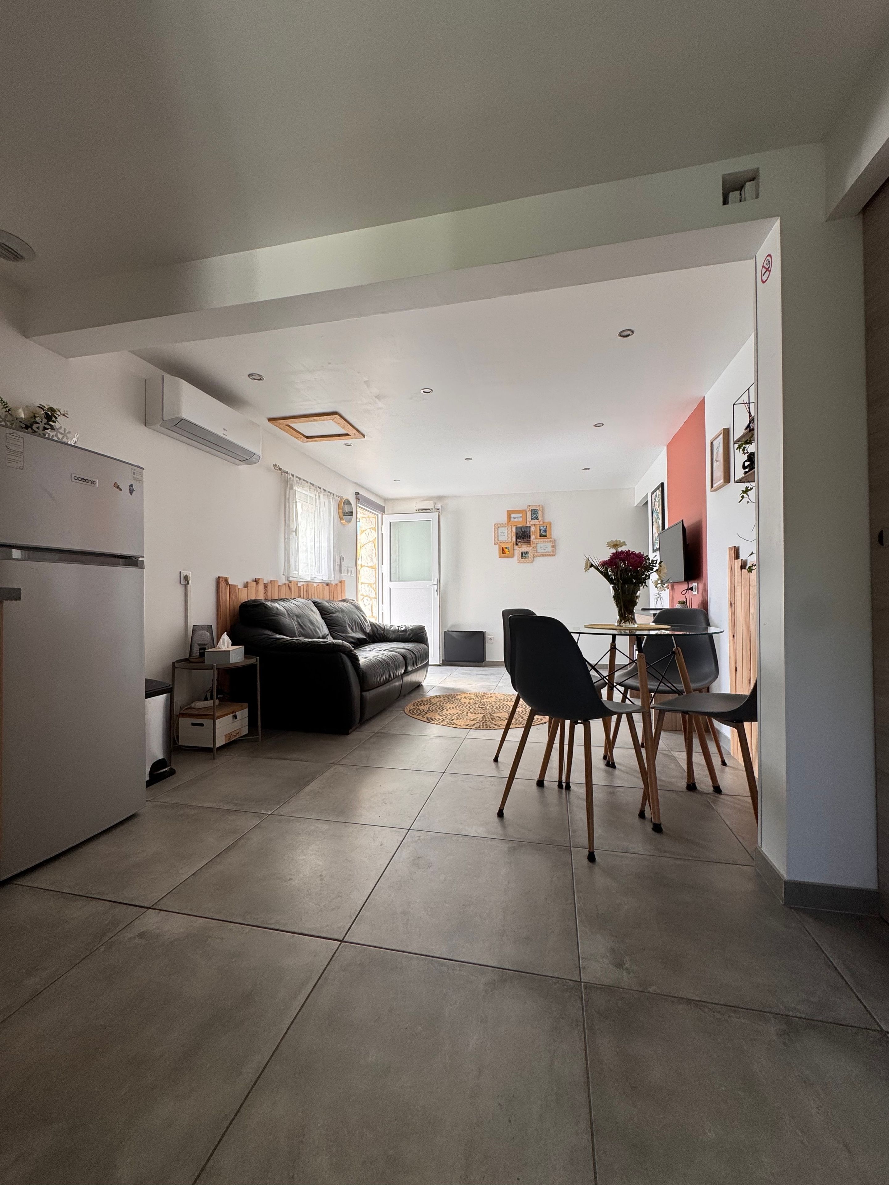 A modern kitchen with a refrigerator, a dining area with a table and chairs, a sofa, and a TV.