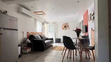 A modern kitchen with a refrigerator, a dining area with a table and chairs, a sofa, and a TV.