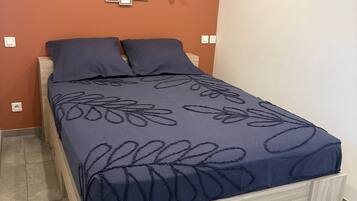 A bedroom with a bed, a wooden nightstand, a wall-mounted light fixture, and a wall decoration.