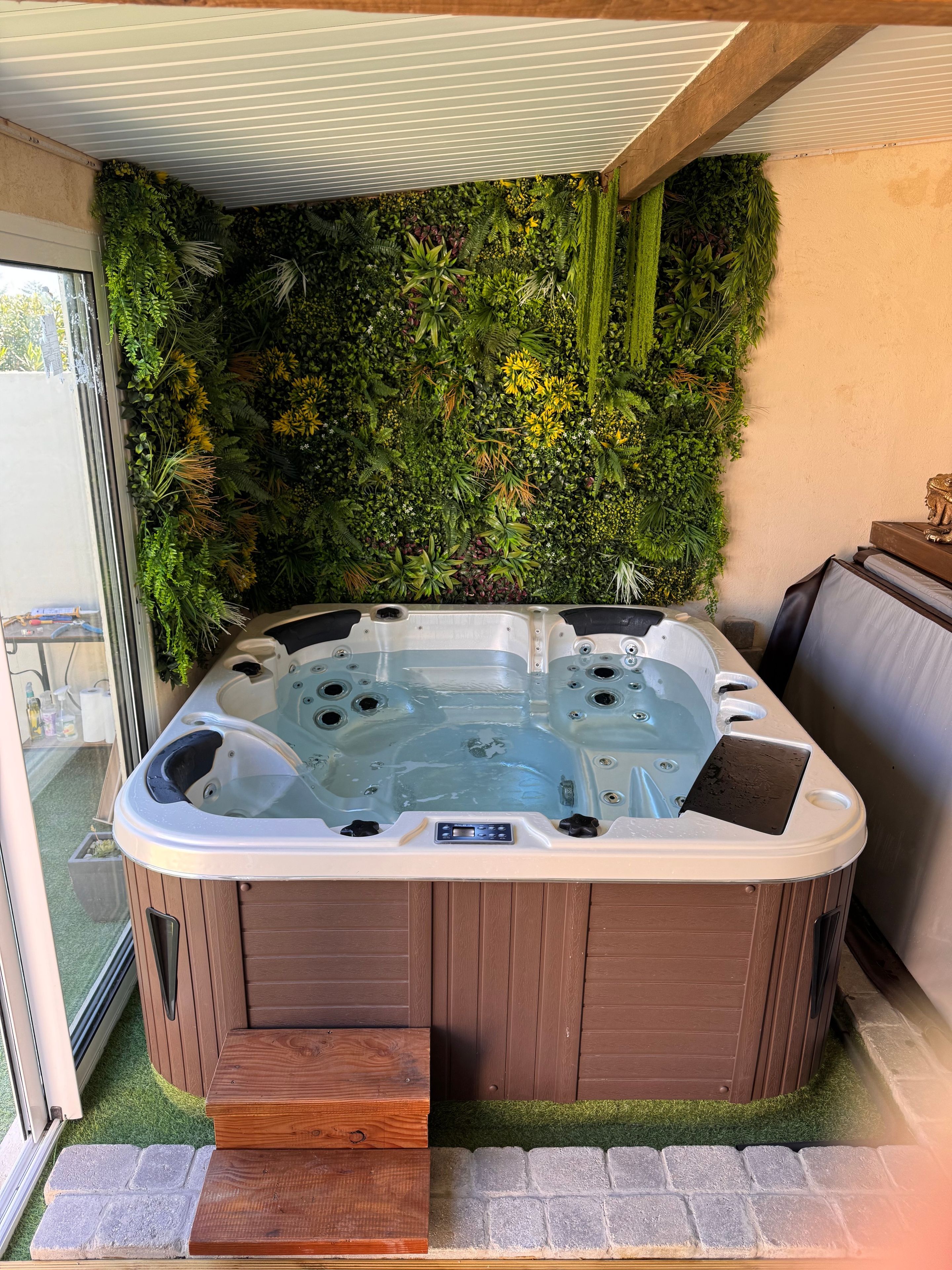 Un bain à remous au revêtement extérieur en bois, entouré d’un mur de verdure luxuriante.