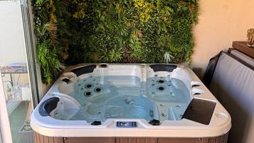 Un bain à remous au revêtement extérieur en bois, entouré d’un mur de verdure luxuriante.
