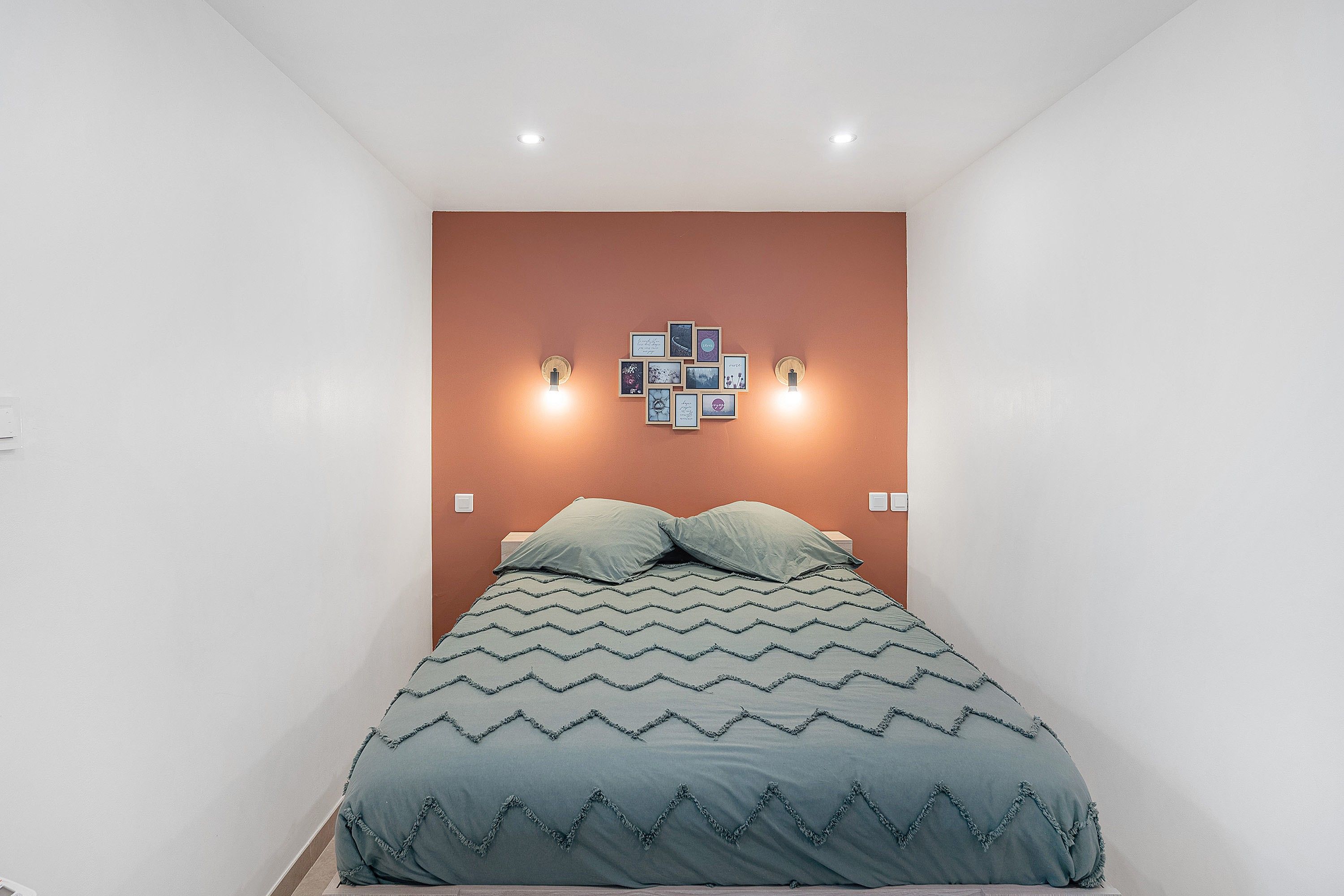 Een slaapkamer met een bed, een wandlamp en een decoratie aan de muur.