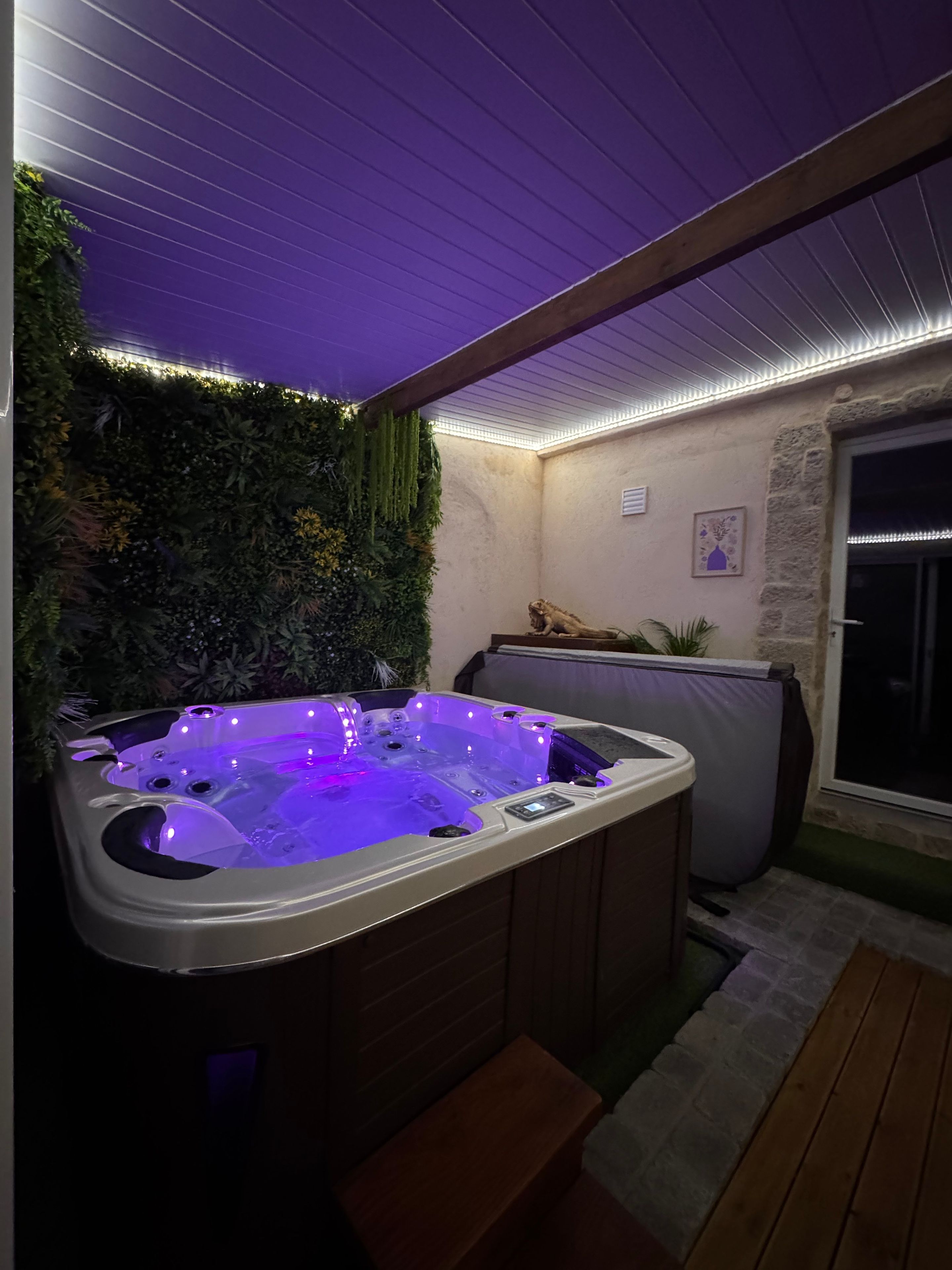 A hot tub with a control panel, surrounded by a wooden deck and a stone wall.