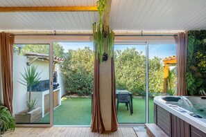 Un espacio exterior moderno con un jacuzzi, una terraza de madera y un ventanal que da a un jardín.