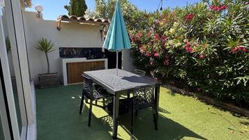 A patio with artificial grass, a table and chairs, a teal umbrella, and a string of lights.