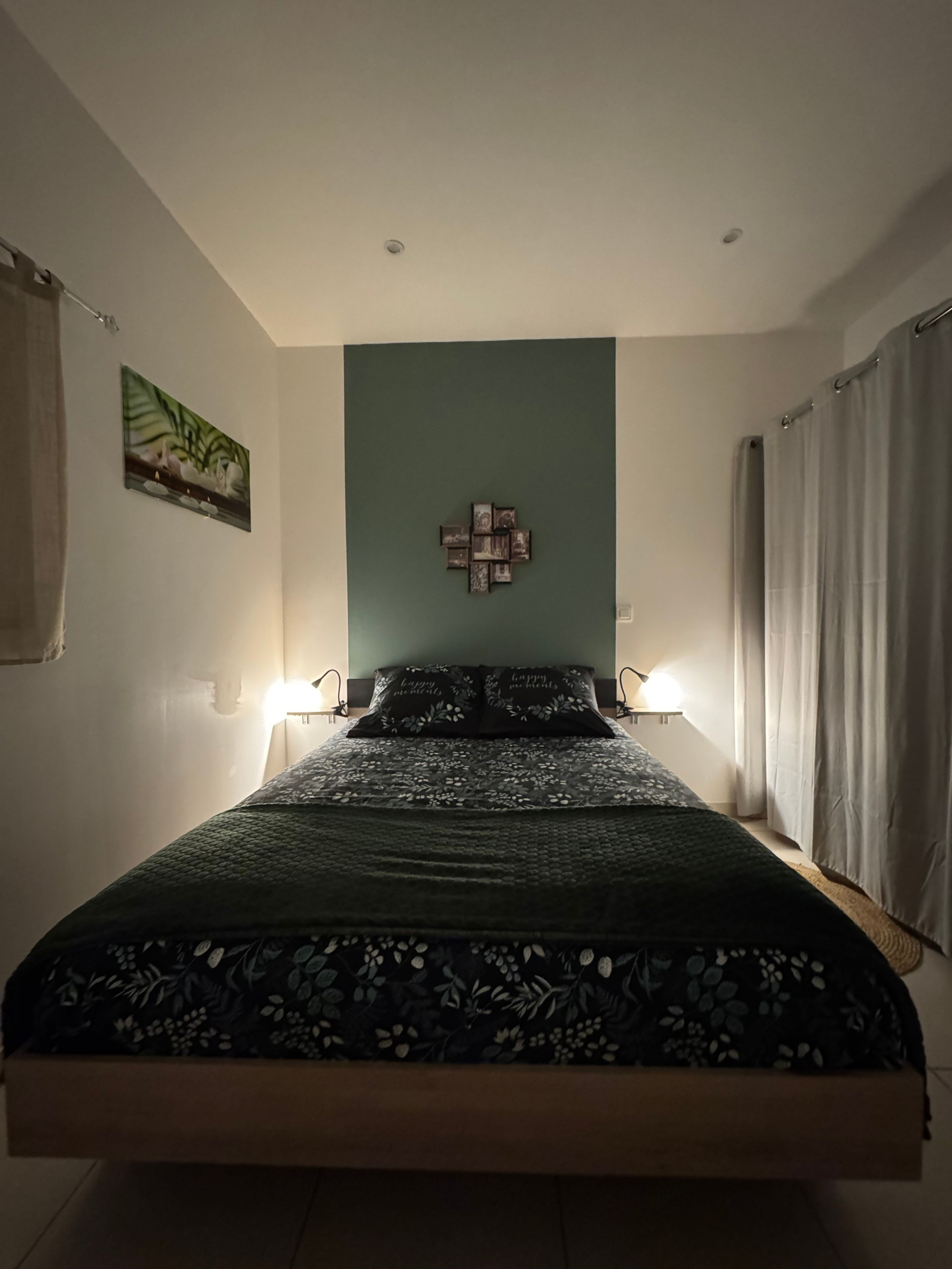 A bedroom with a bed, two bedside lamps, a wall-mounted picture, and a curtain.