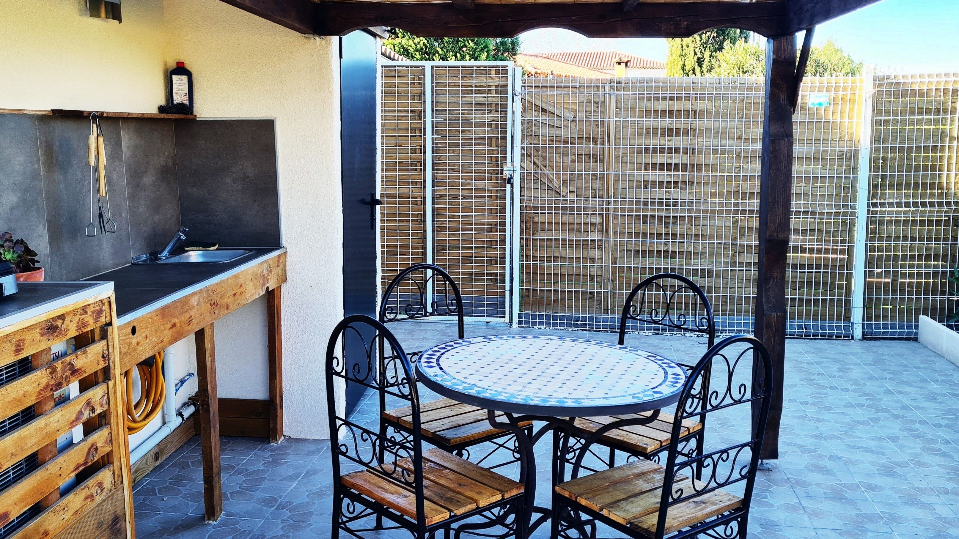 An outdoor patio with a round table and chairs, a wooden bench, and a grill.