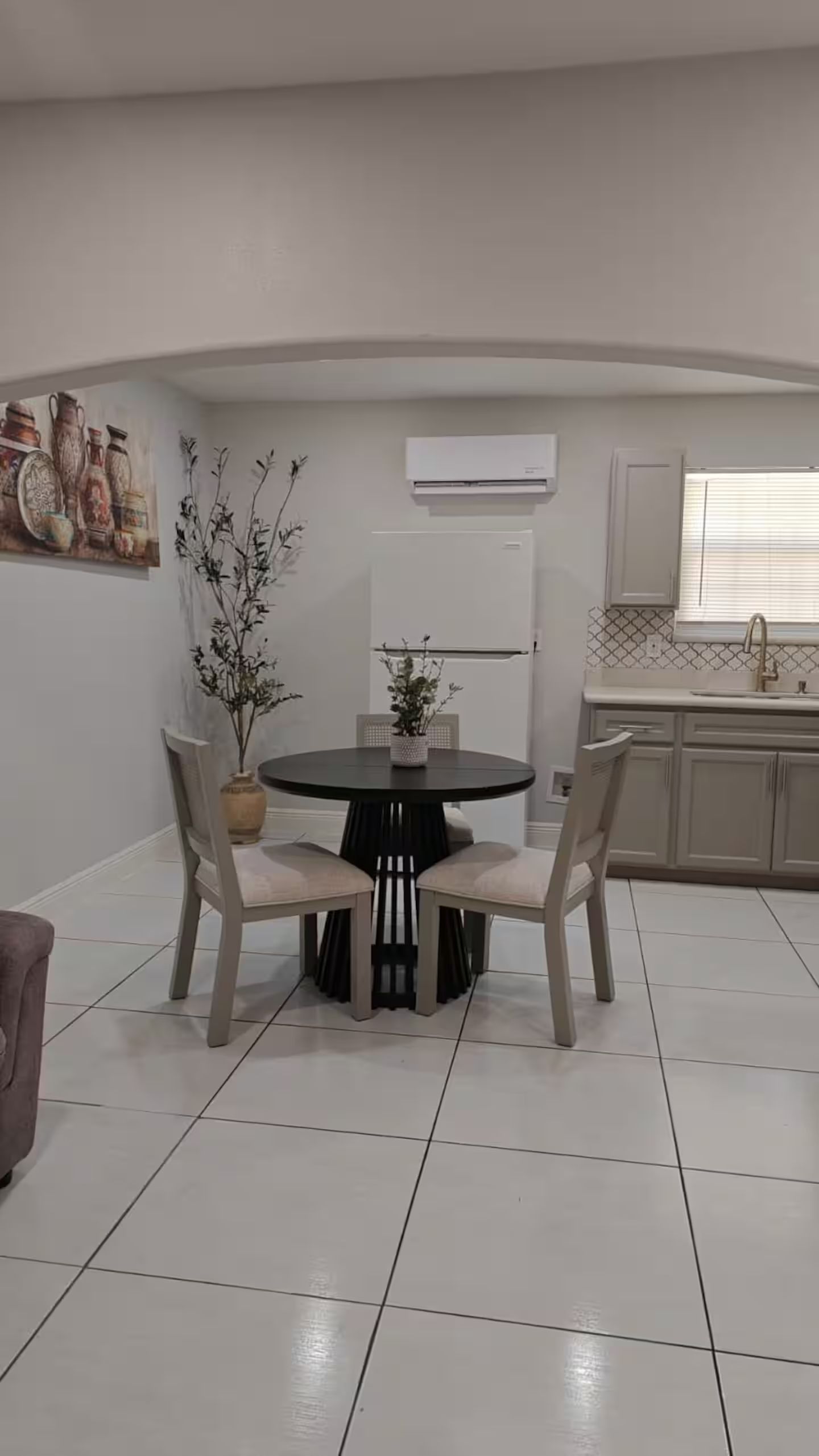 A dining area with a round table and chairs, a potted plant, and a kitchen in the background.