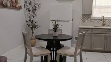 A dining area with a round table and chairs, a potted plant, and a kitchen in the background.