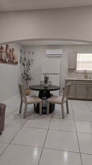 A dining area with a round table and chairs, a potted plant, and a kitchen in the background. - 1717 Apartment (Laredo)