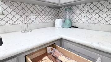 A kitchen with white cabinets, a patterned backsplash, and a drawer containing wooden utensils.