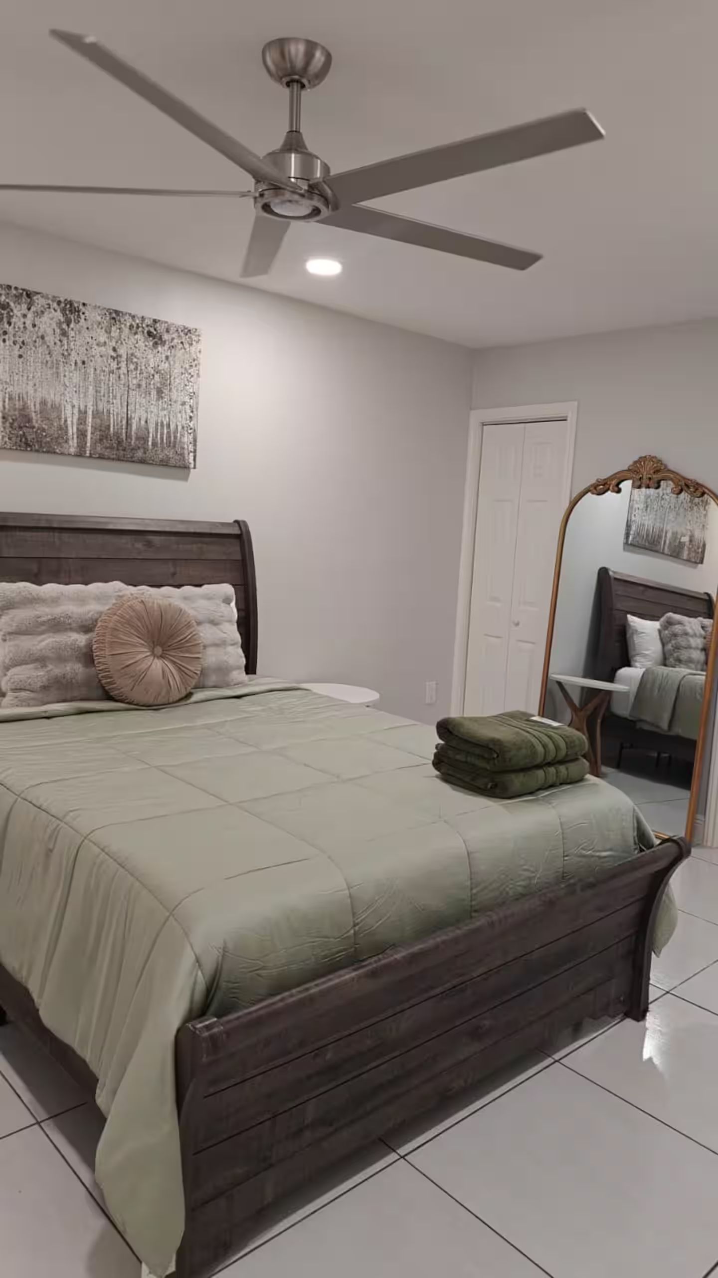 A bedroom with a bed, a ceiling fan, a large mirror, and a door.