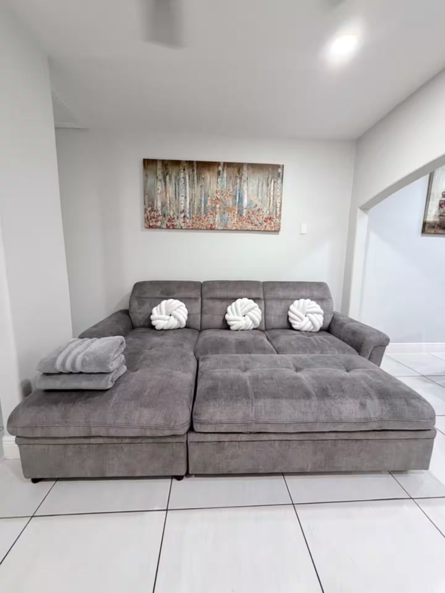 A grey sectional sofa with three white, twisted pillows and a grey throw blanket.
