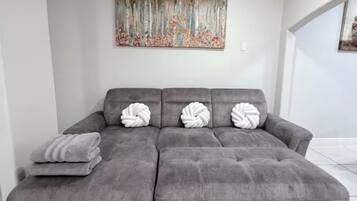A grey sectional sofa with three white, twisted pillows and a grey throw blanket.