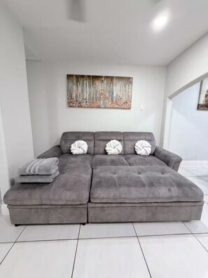 A grey sectional sofa with three white, twisted pillows and a grey throw blanket. - 1717 Apartment (Laredo)