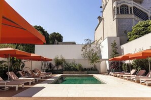 Ein Poolbereich mit Liegestühlen und Sonnenschirmen, umgeben von einer niedrigen Mauer und viel Grün.