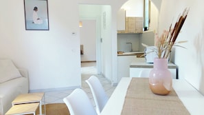 Una sala de estar moderna con un sofá, una mesa de comedor con sillas y una cocina con pileta y alacenas.