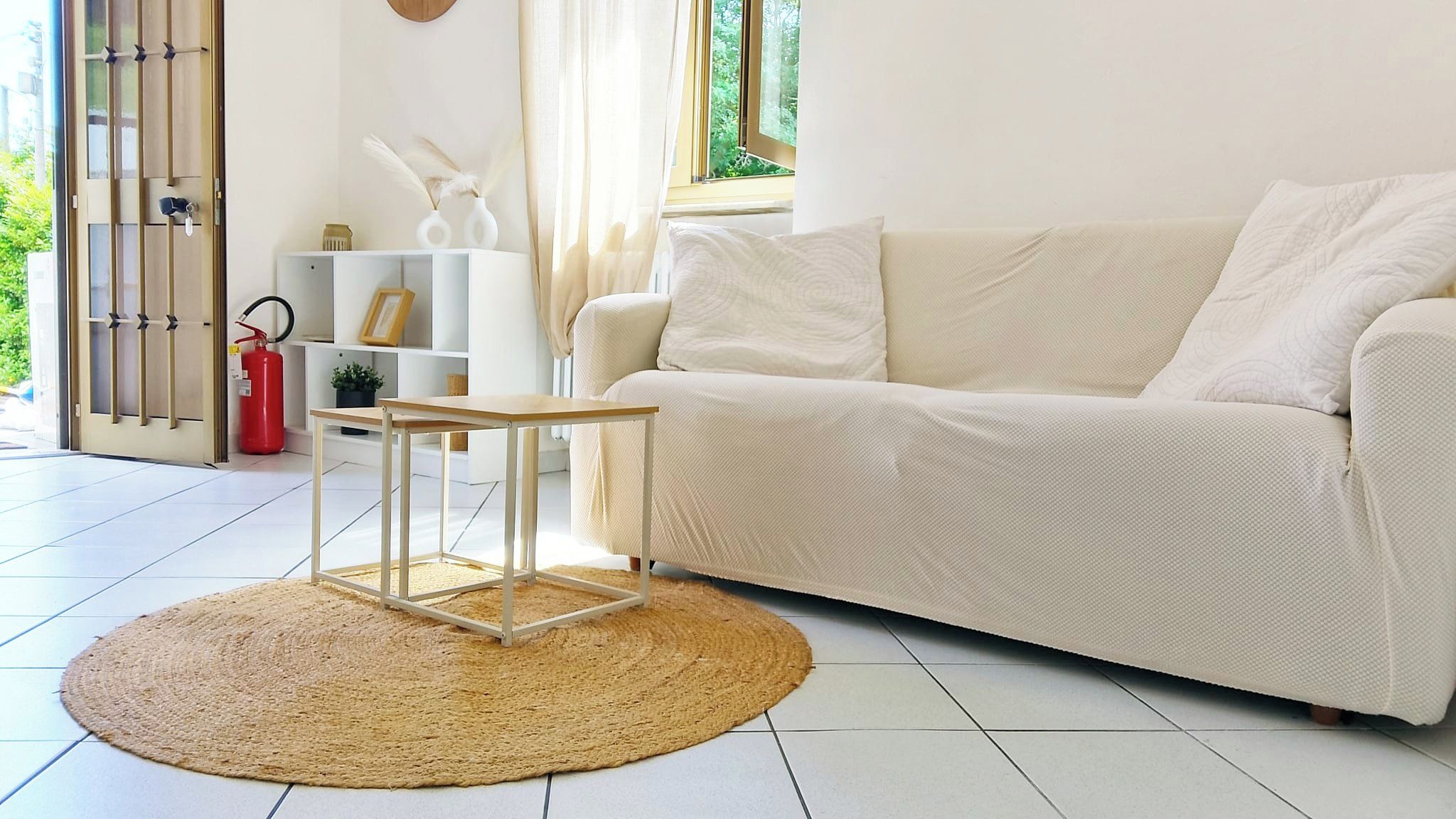 A living room with a white sofa, a small wooden table, a woven rug, and a fire extinguisher.