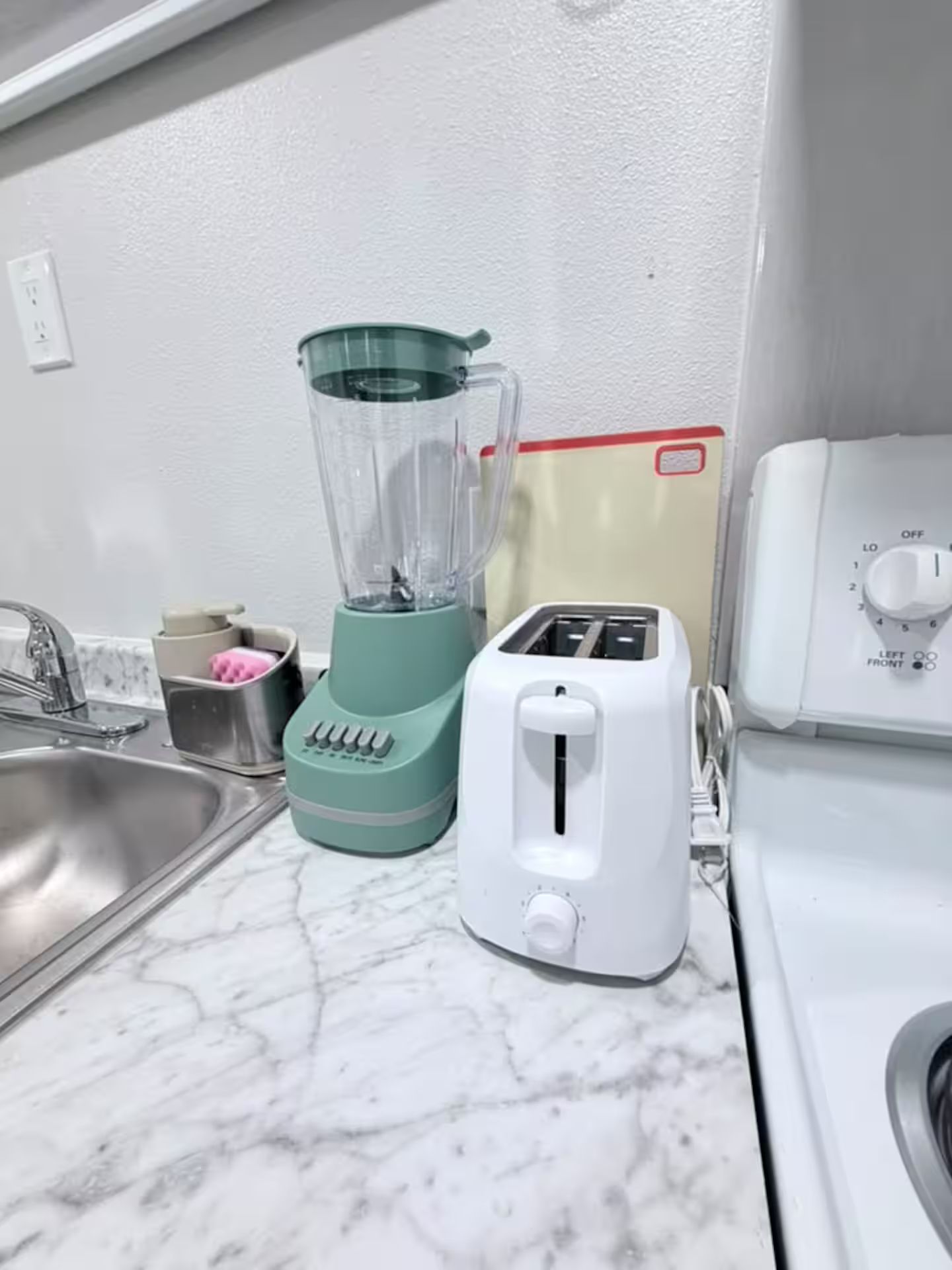 A kitchen with a blender, toaster, and a white stove.