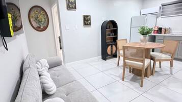 A modern living room with a sofa, dining table, chairs, and a kitchen area.