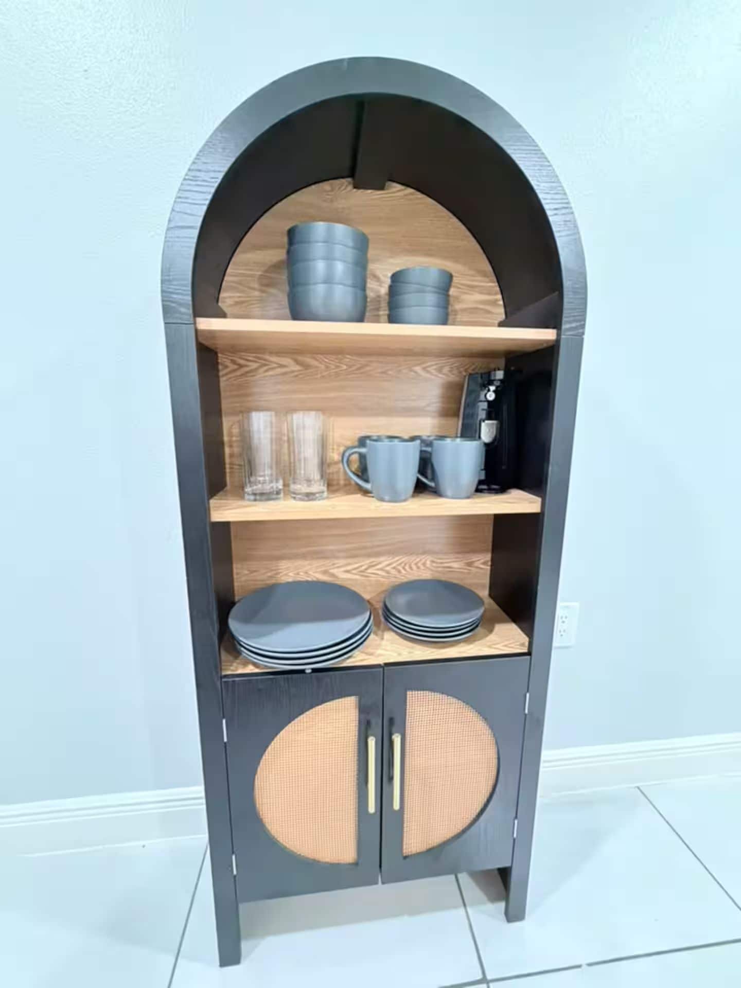 A dark-colored, arched display cabinet with multiple shelves, containing various items like cups, glasses, and plates.