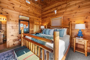 Innenansicht einer Holzhütte mit einem Bett, Nachttischen, einem Spiegel und einem aufgehängten Kuhschädel.