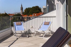 Ein Balkon mit zwei Liegestühlen, einem kleinen Tisch und einem weißen Geländer.