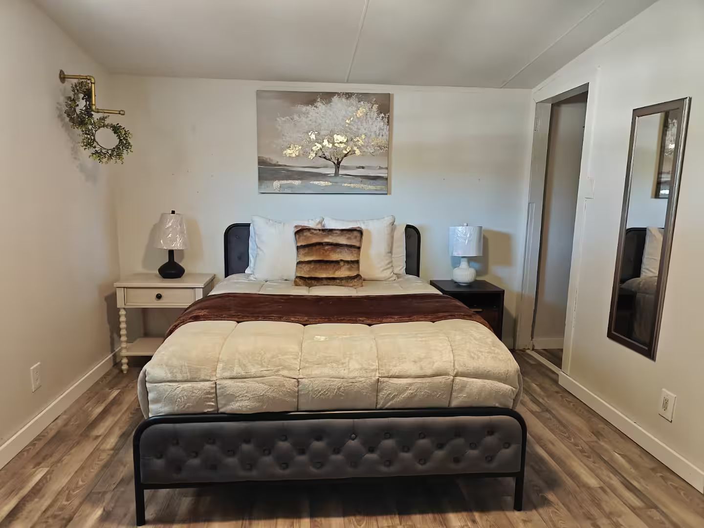 Une chambre à coucher comprenant un lit, deux tables de chevet, une lampe fixée au mur, un tableau et un miroir.
