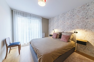 Un dormitorio con una cama, una silla, una mesita de noche y una pared con estampado floral.