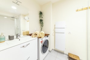 A bathroom with a white sink, mirror, and a washing machine. - Le B3 de Claire (Mont-Dore)