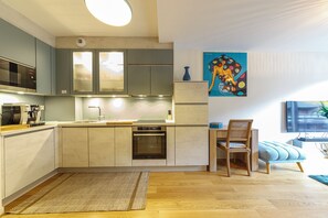 Una cocina moderna con electrodomésticos integrados, un comedor con mesa y sillas de madera, y un cuadro abstracto de colores en la pared.