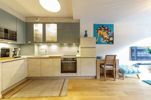 Una cocina moderna con electrodomésticos integrados, un comedor con mesa y sillas de madera, y un cuadro abstracto de colores en la pared.