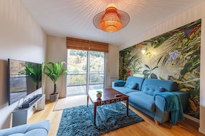 A living room with a sofa, a coffee table, a TV, and a large window. - Le B3 de Claire (Mont-Dore)