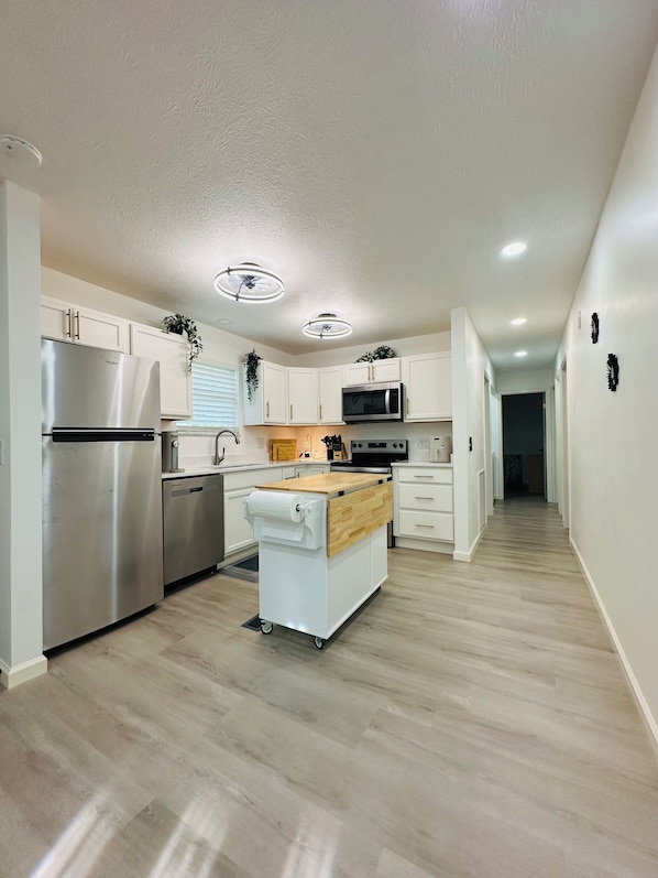 A modern kitchen with white cabinetry, stainless steel appliances, and a central island with a wooden countertop.