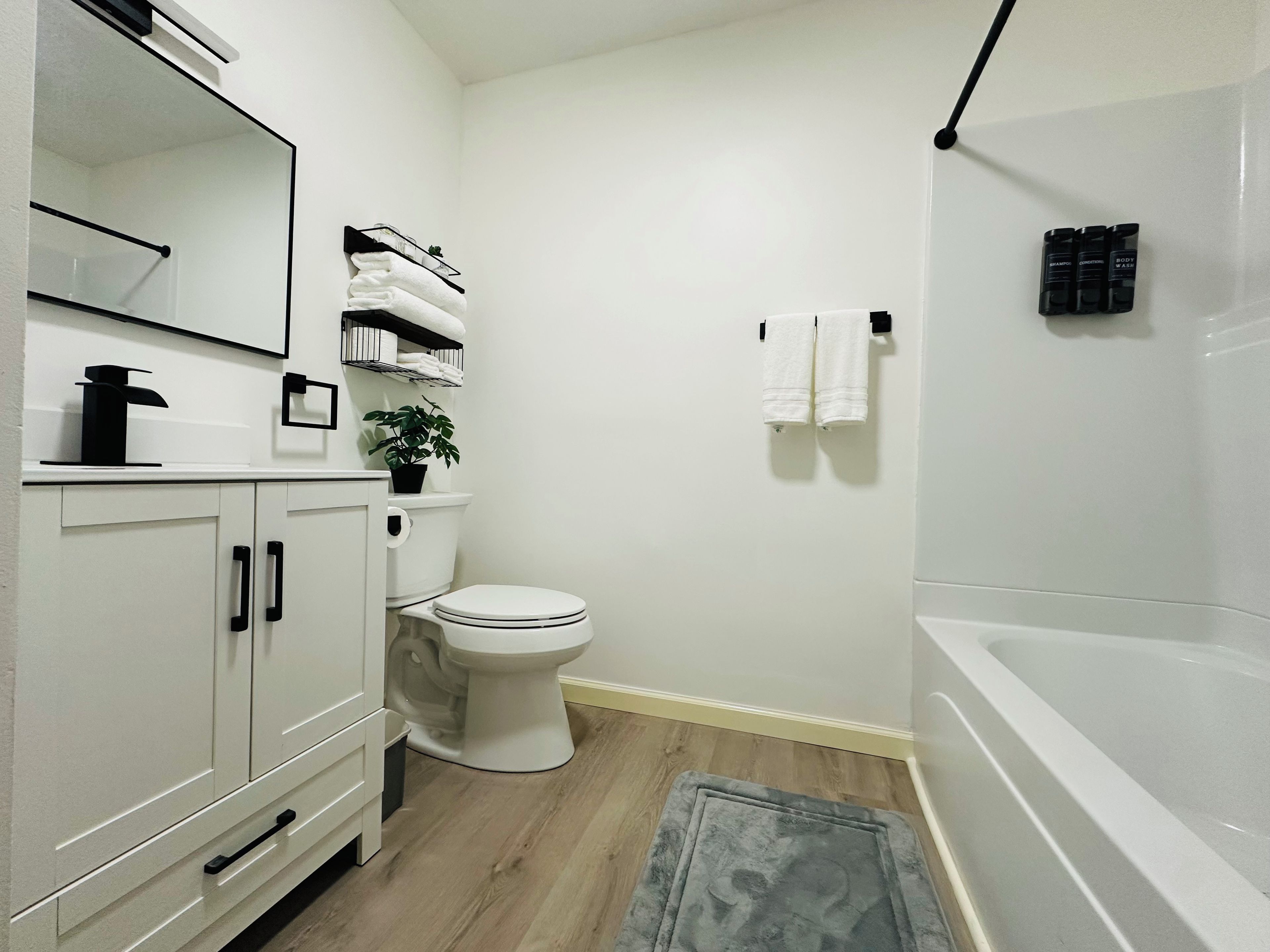 Un baño con inodoro, lavabo y bañera. Hay un perchero con toallas y una planta en el lavabo.
