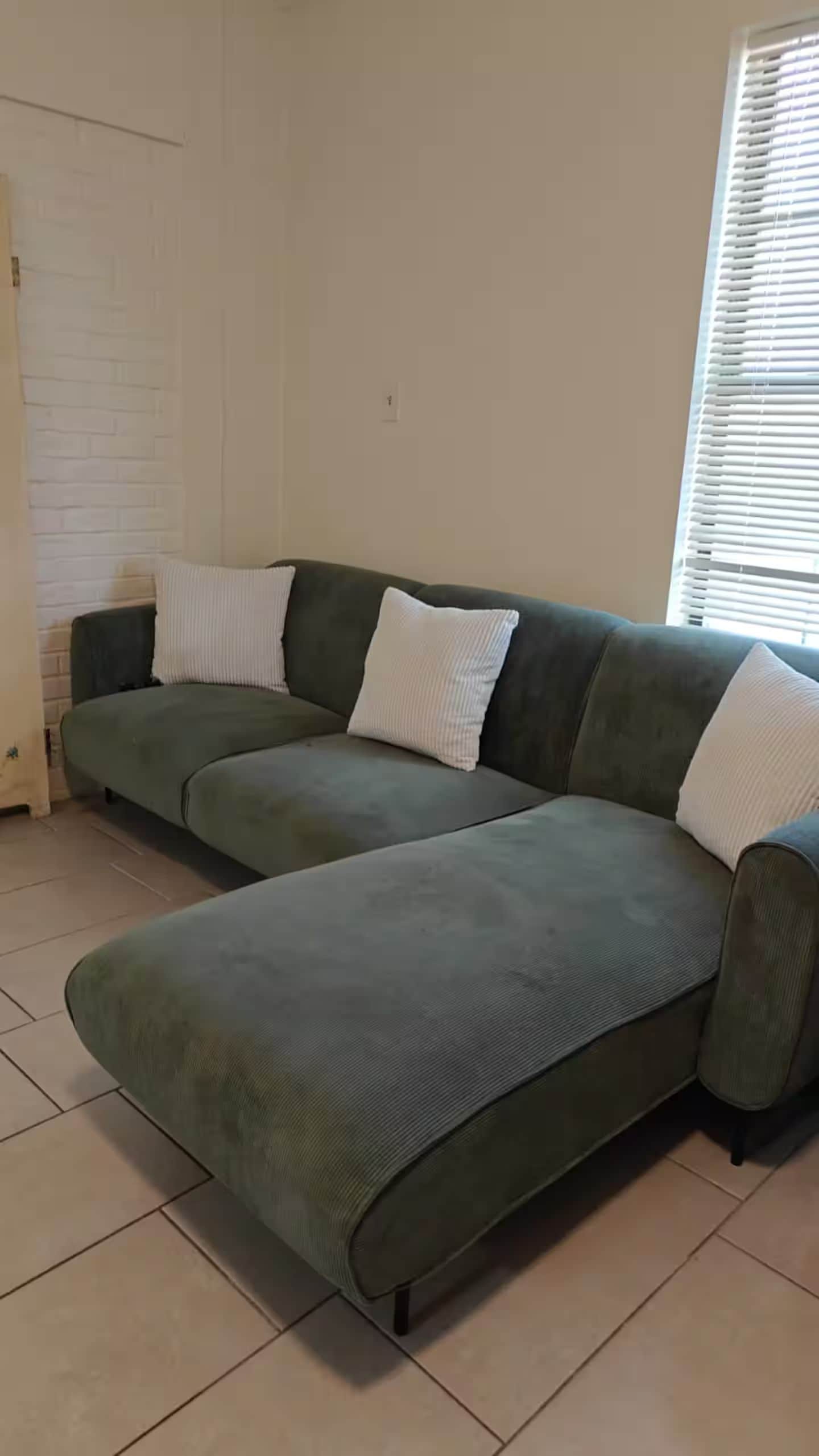Un canapé modulable recouvert d’un tissu texturé, placé dans une pièce dont le sol est carrelé et un des murs est en briques blanches.
