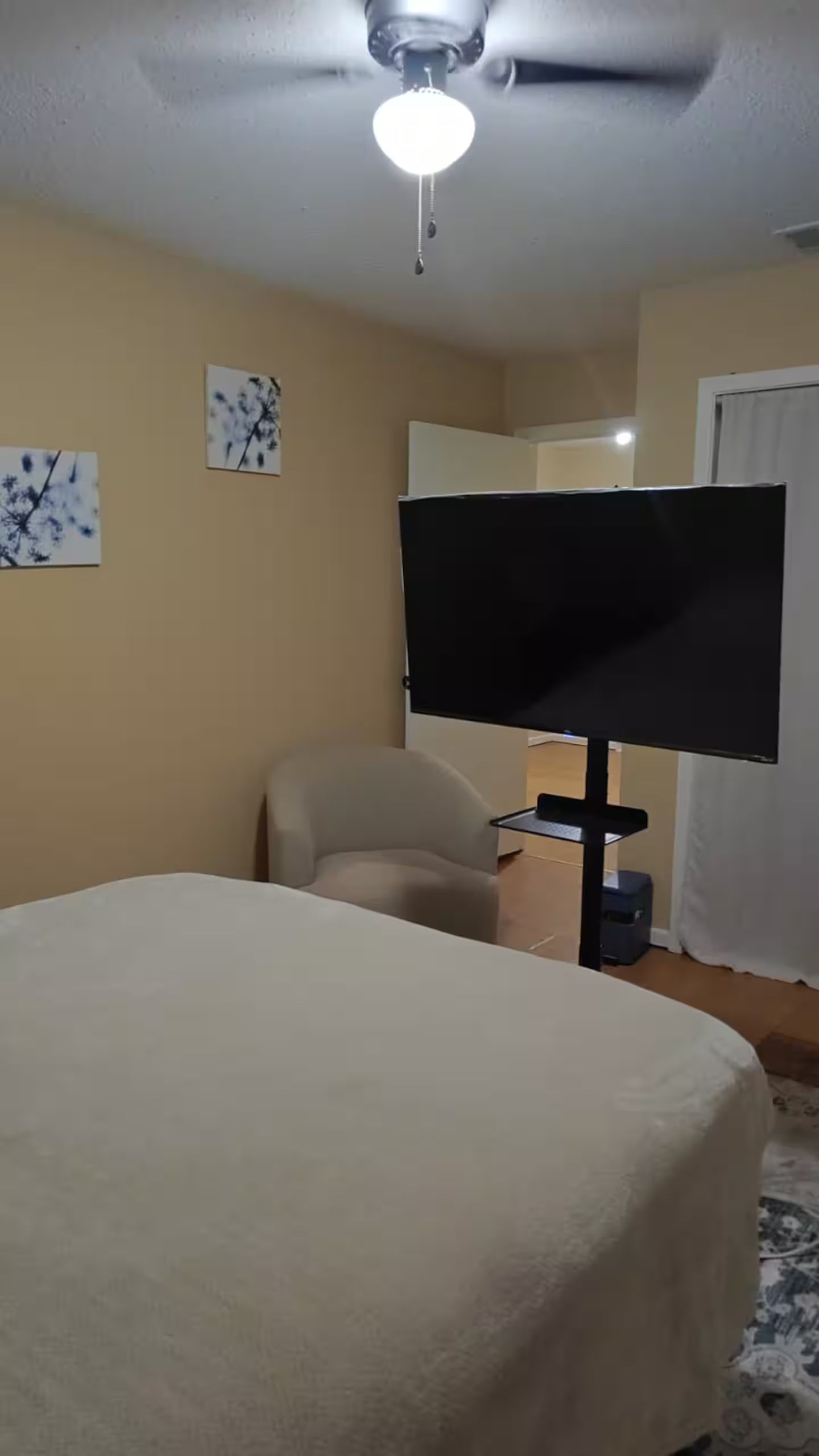Una habitación de hotel con una cama, una silla, un televisor y obras de arte en las paredes.
