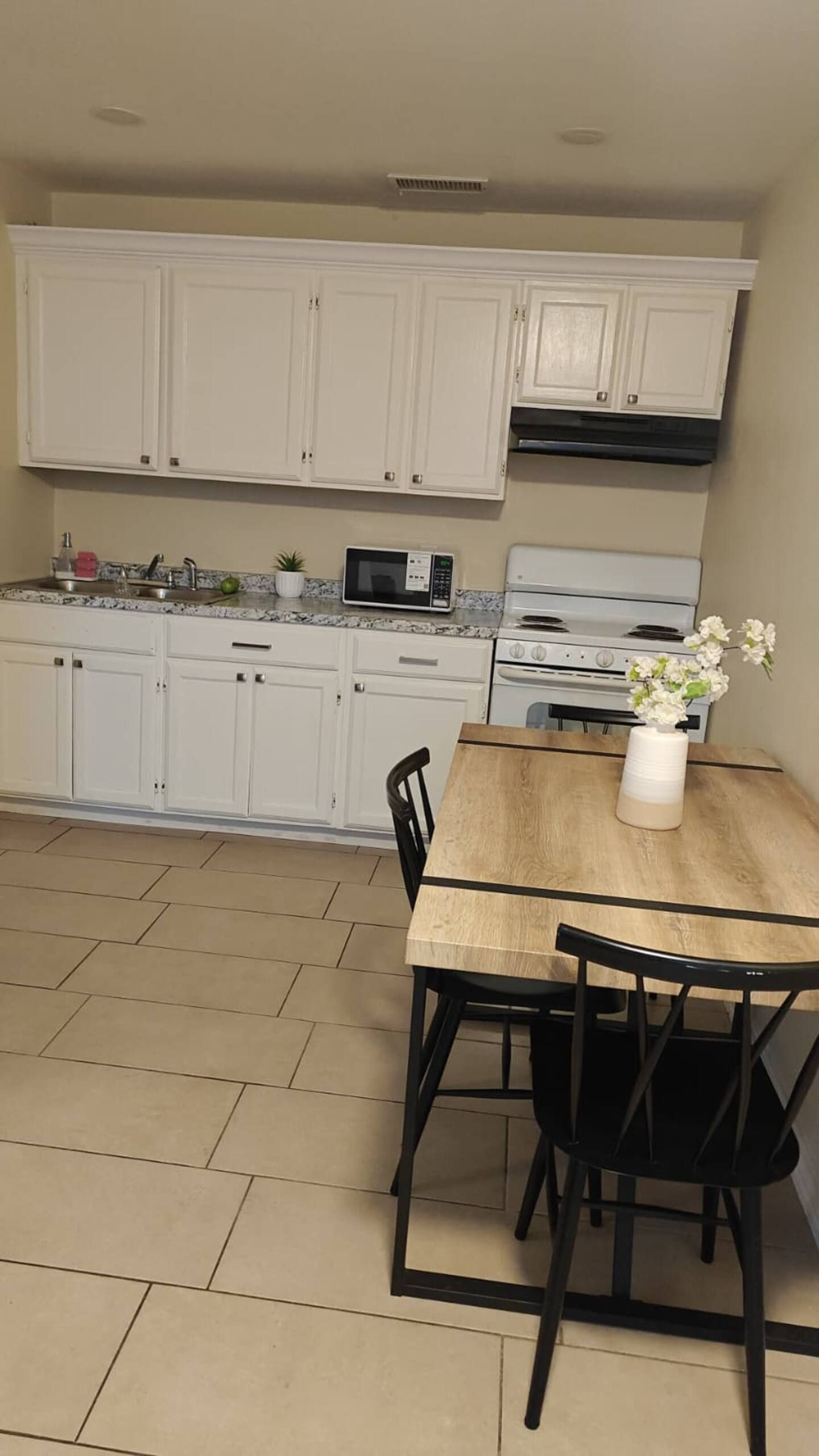 Une cuisine avec des meubles blancs, un four à micro-ondes, une cuisinière et une table à manger avec des chaises.