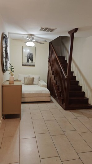 Una camera da letto con un letto, un comodino, una ventola a soffitto, una scala e un quadro appeso al muro.