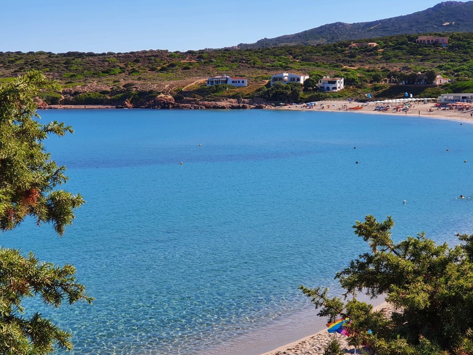 Una spiaggia costiera con acqua cristallina, una riva sabbiosa e edifici sullo sfondo.