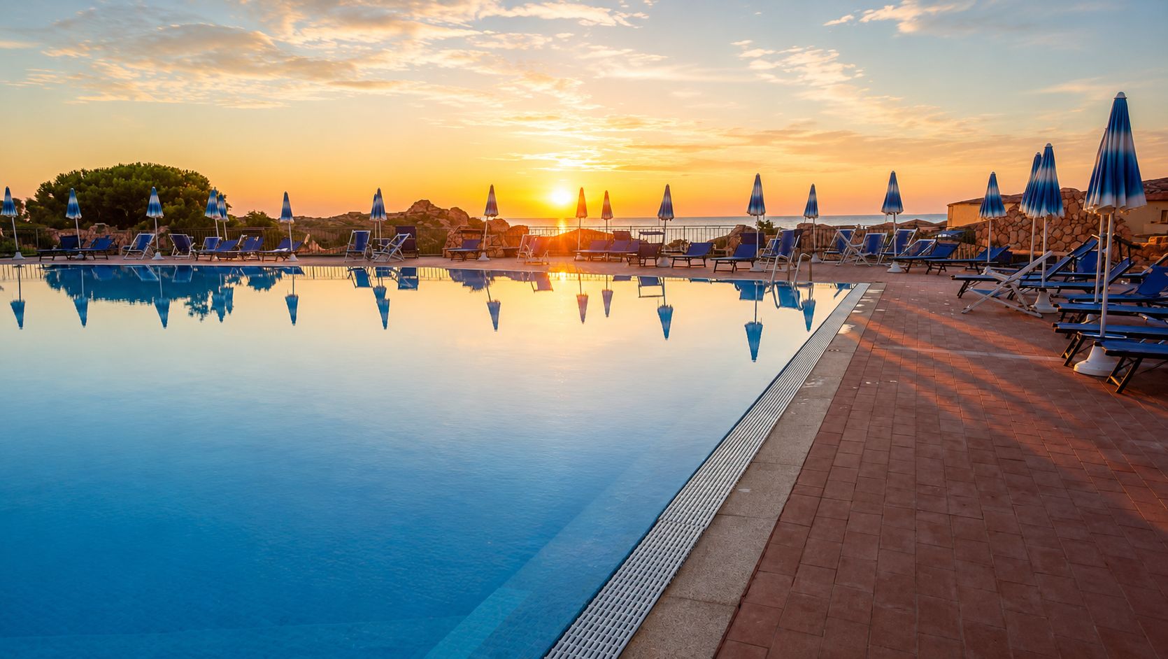 Een zwembad met ligbedden en parasols, dat de zonsondergang weerspiegelt.