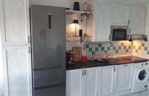A compact kitchen with a refrigerator, microwave, and washing machine. - Beach Home in Sardegna Italy - Wake Up in Heaven! (Canneddi)